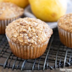 A muffin with oatmeal topping on a cooling rack with fresh pears in the back.