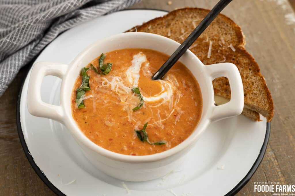A bowl of creamy tomato soup with basil and parmesan cheese on top.