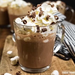 A glass mug with hot chocolate made from scratch topped with heavy cream and chocolate curls.