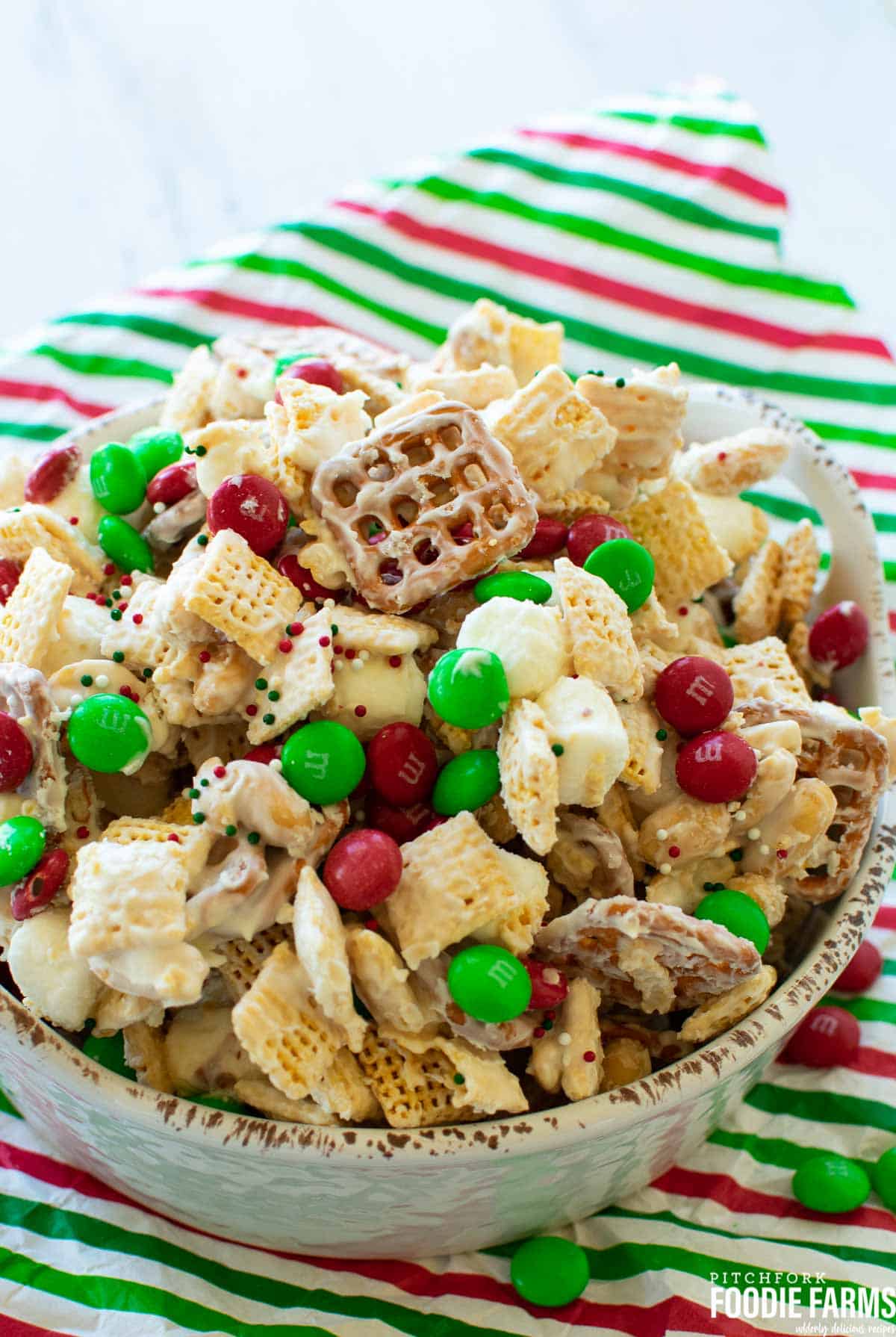 Snack mix made with Chex cereal, pretzels, and M&Ms coated in white chocolate in a bowl.