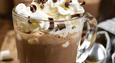 A glass mug of hot chocolate with whipped cream and chocolate chips on top.