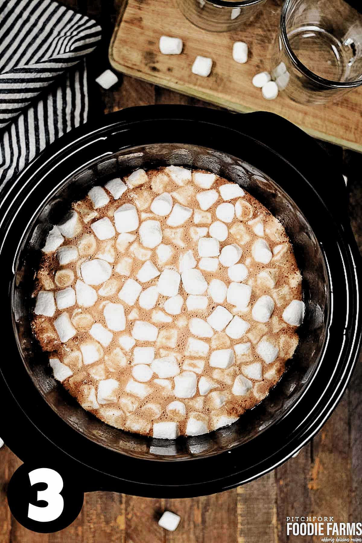 Hot chocolate made in a slow cooker topped with marshmallows.