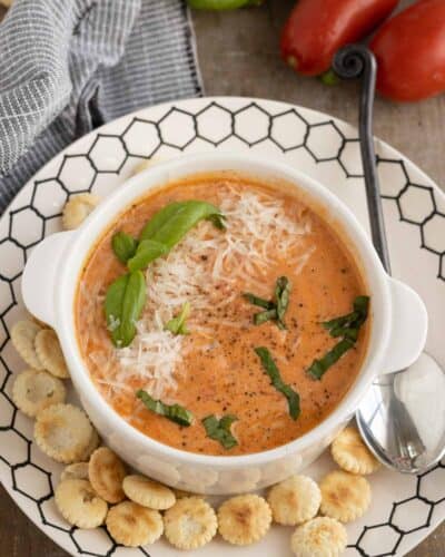 Creamy tomato soup with basil and fresh tomatoes in the background.