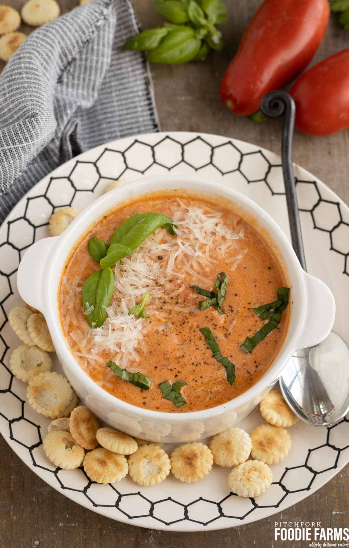 Creamy tomato soup with basil and fresh tomatoes in the background.