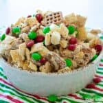 A white bowl with Christmas Chex Mix covered in white chocolate and with M&Ms.