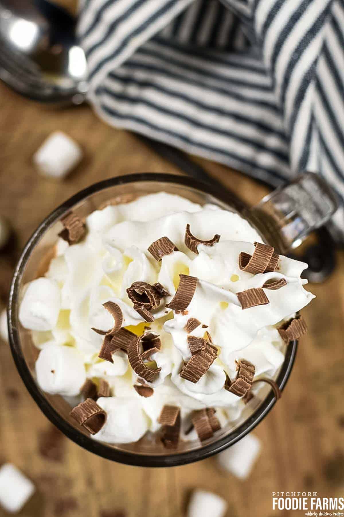 A top view of a mug of hot chocolate topped with milk chocolate curls and heavy whipped cream.