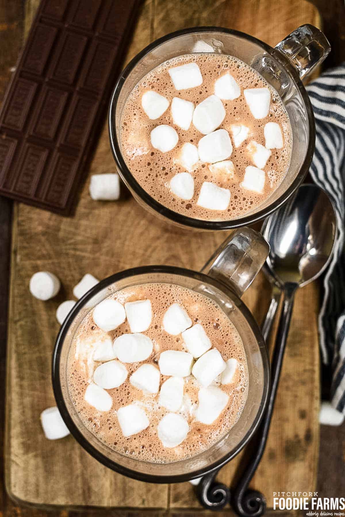 Two glass mugs with hot chocolate topped with marshmallows.