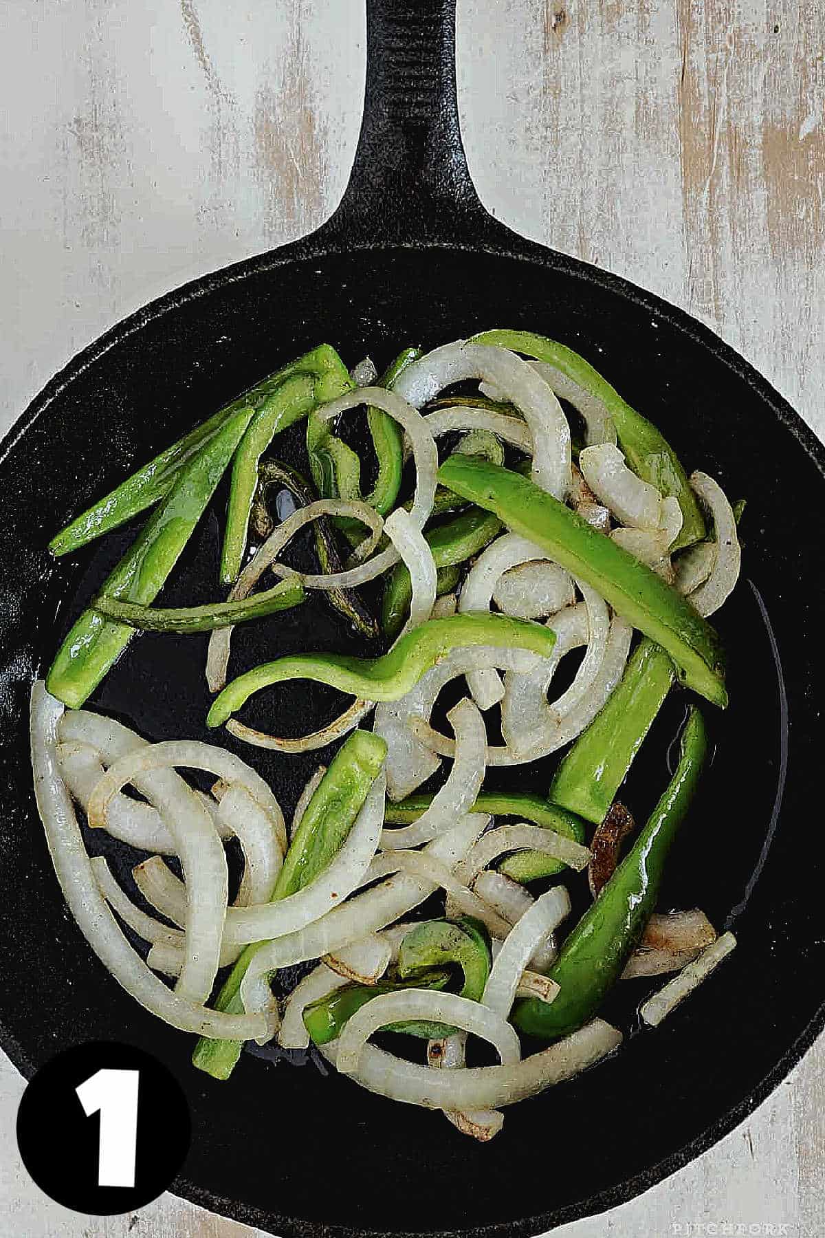 A cast iron skillet with sliced onions and green peppers. 