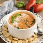 A bowl of creamy tomato soup with cheese, basil, and crackers.