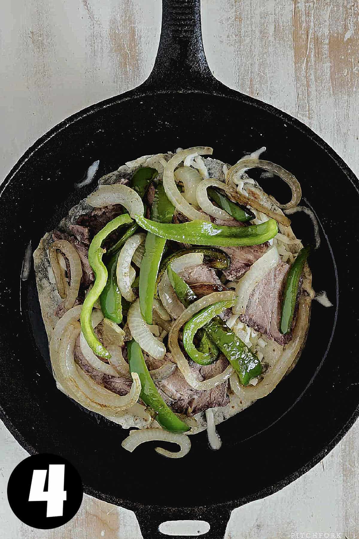 A flour tortilla in a skillet, topped with green peppers and onions.