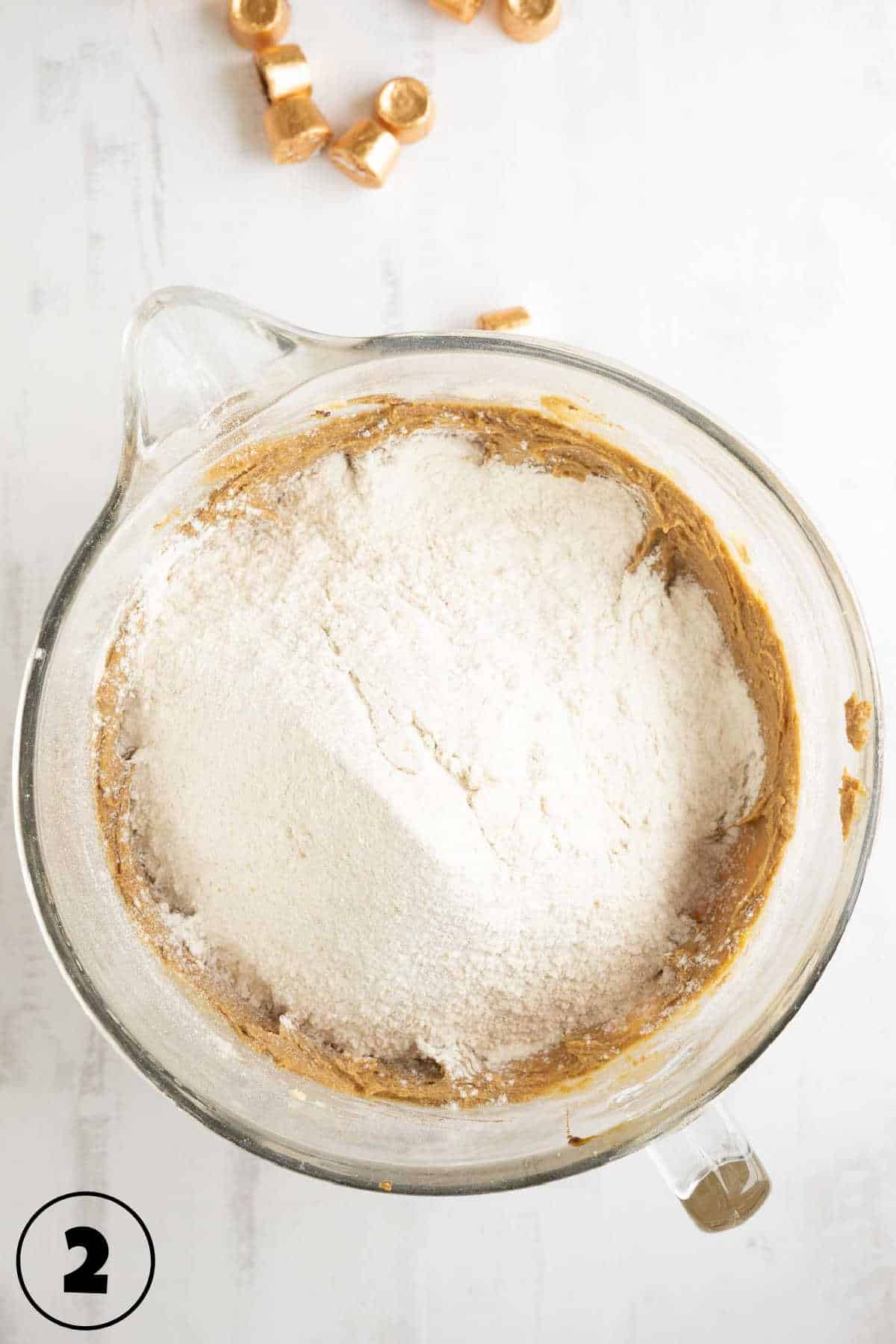 A glass mixing bowl with flour sprinkled on top of creamed butter and sugar.