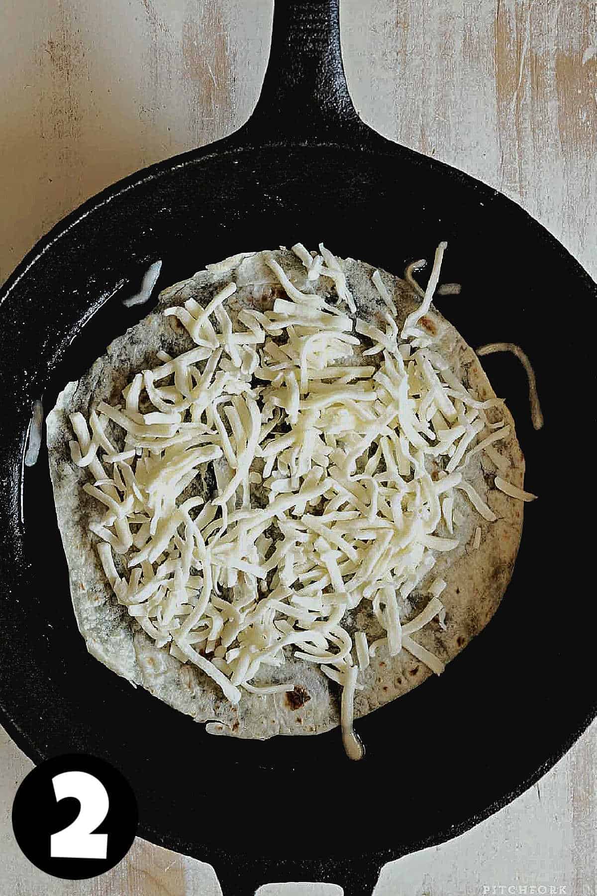 A flour tortilla topped with grated mozzarella cheese in a skillet.