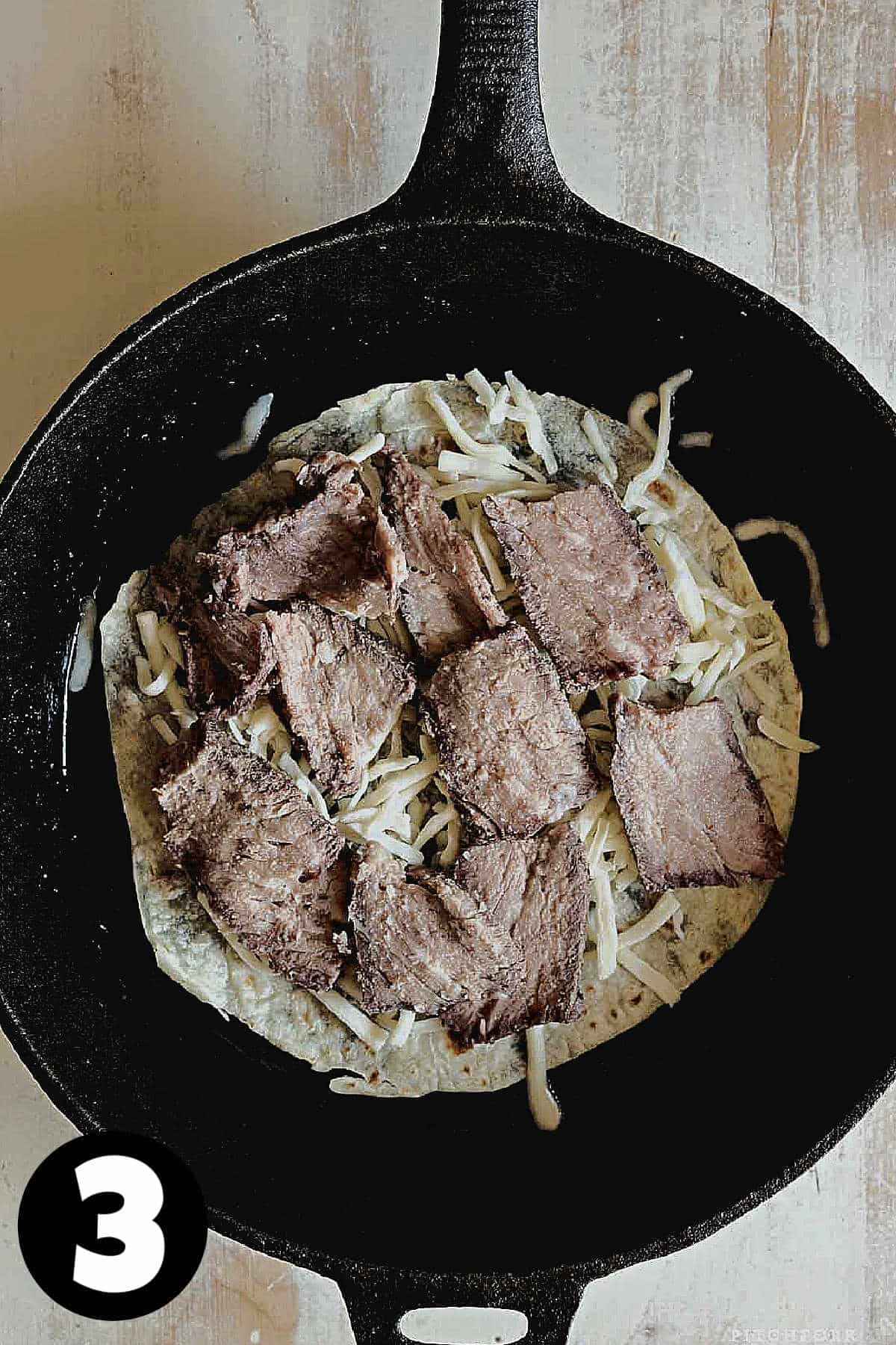 A flour tortilla topped with steak and grated cheese.