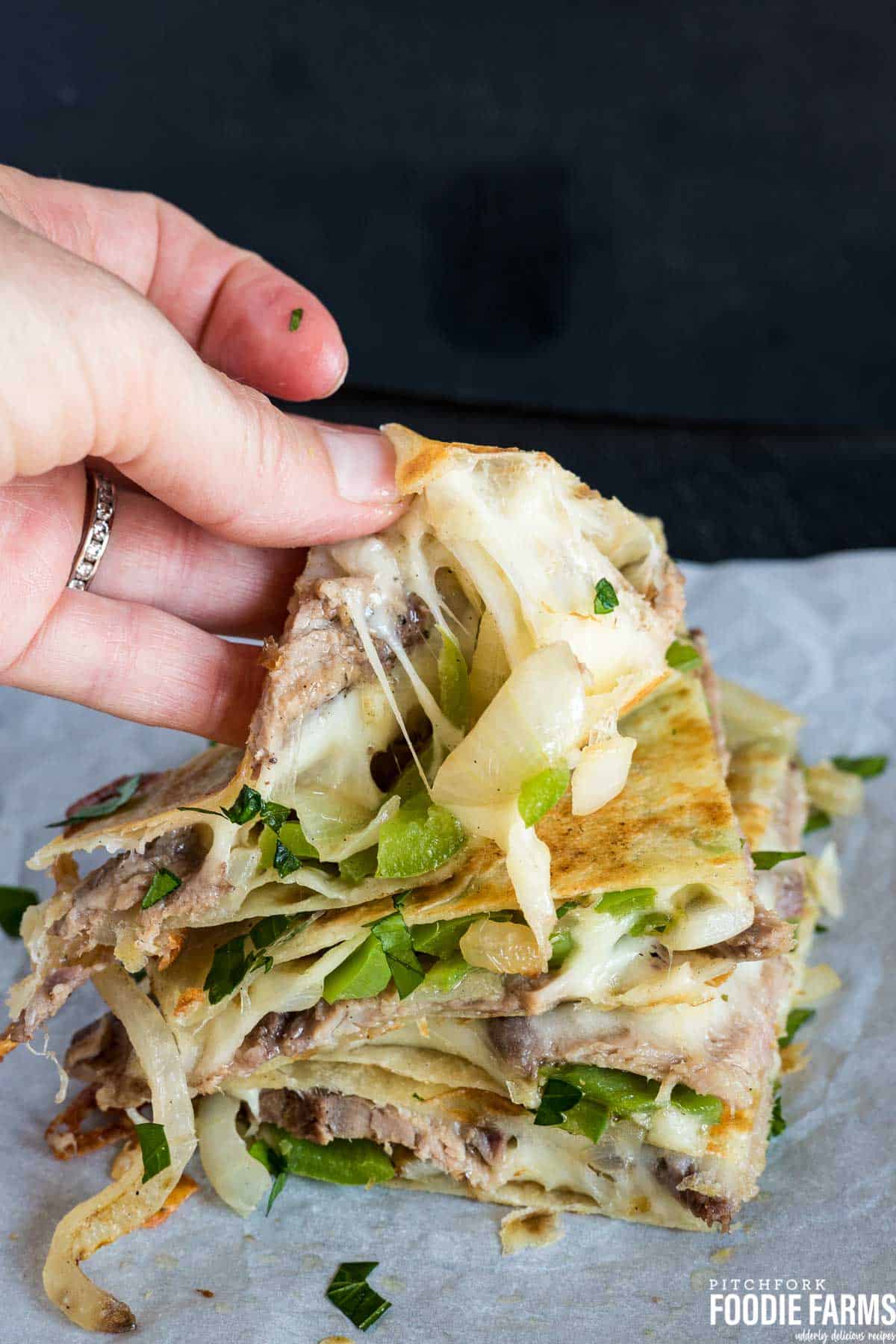 A Philly Cheese Steak Quesadilla being pulled apart with melted cheese being pulled.