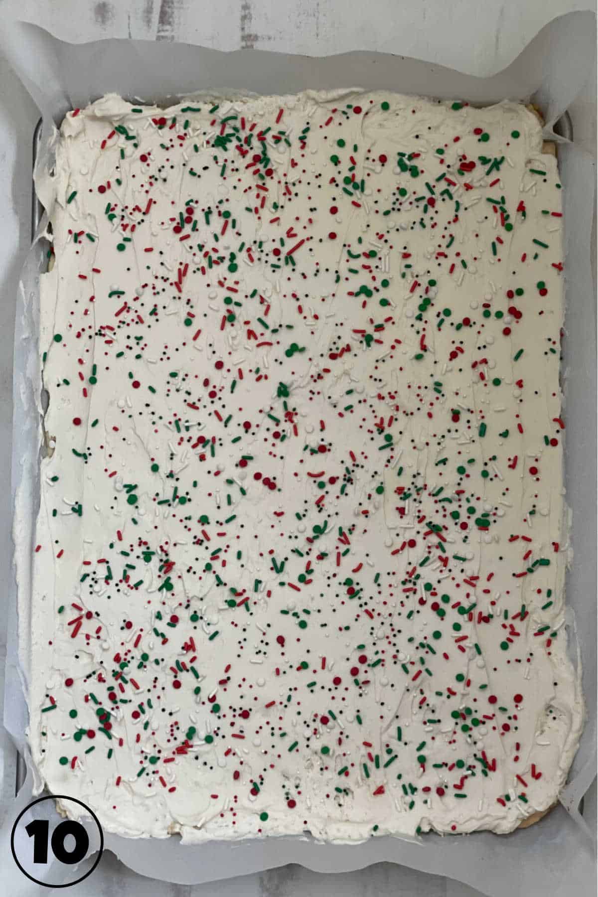 Sugar cookie bars with white frosting and red and green sprinkles in a sheetpan.