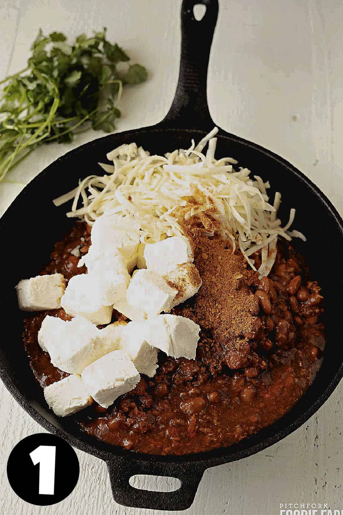 Cream cheese cubes with chili and grated cheese in a skillet.