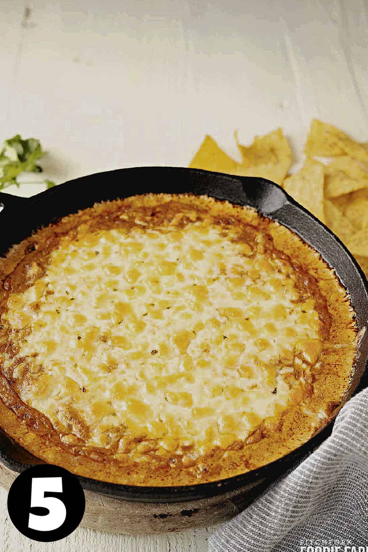 Cheesy chili dip with melted cheese in a skillet.