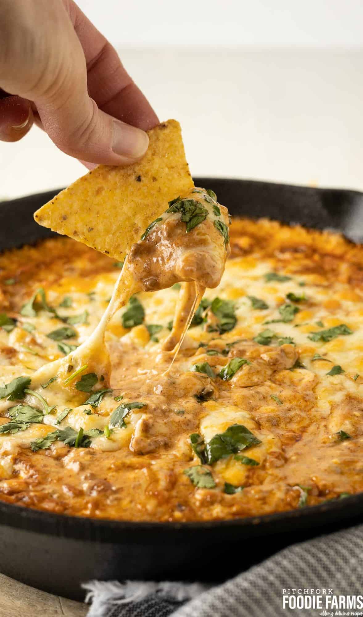 A cast iron skillet with a tortilla chip getting a scoop of chili cheese dip.