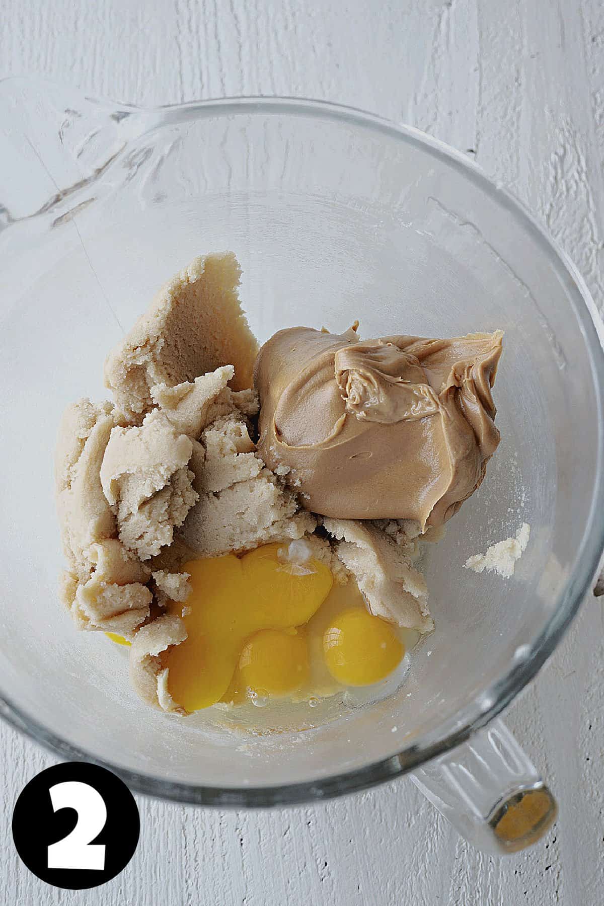 A KitchenAid mixing bowl with creamed butter and sugar and peanut butter and eggs to make cookies.