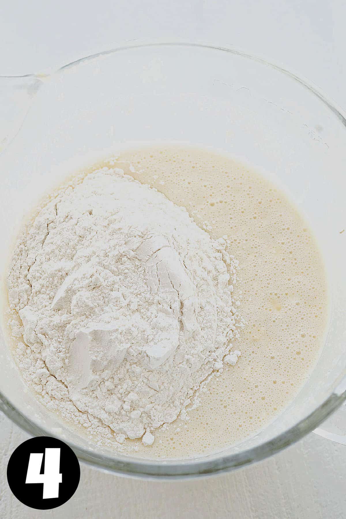 Wet ingredients with flour on top in a mixing bowl.