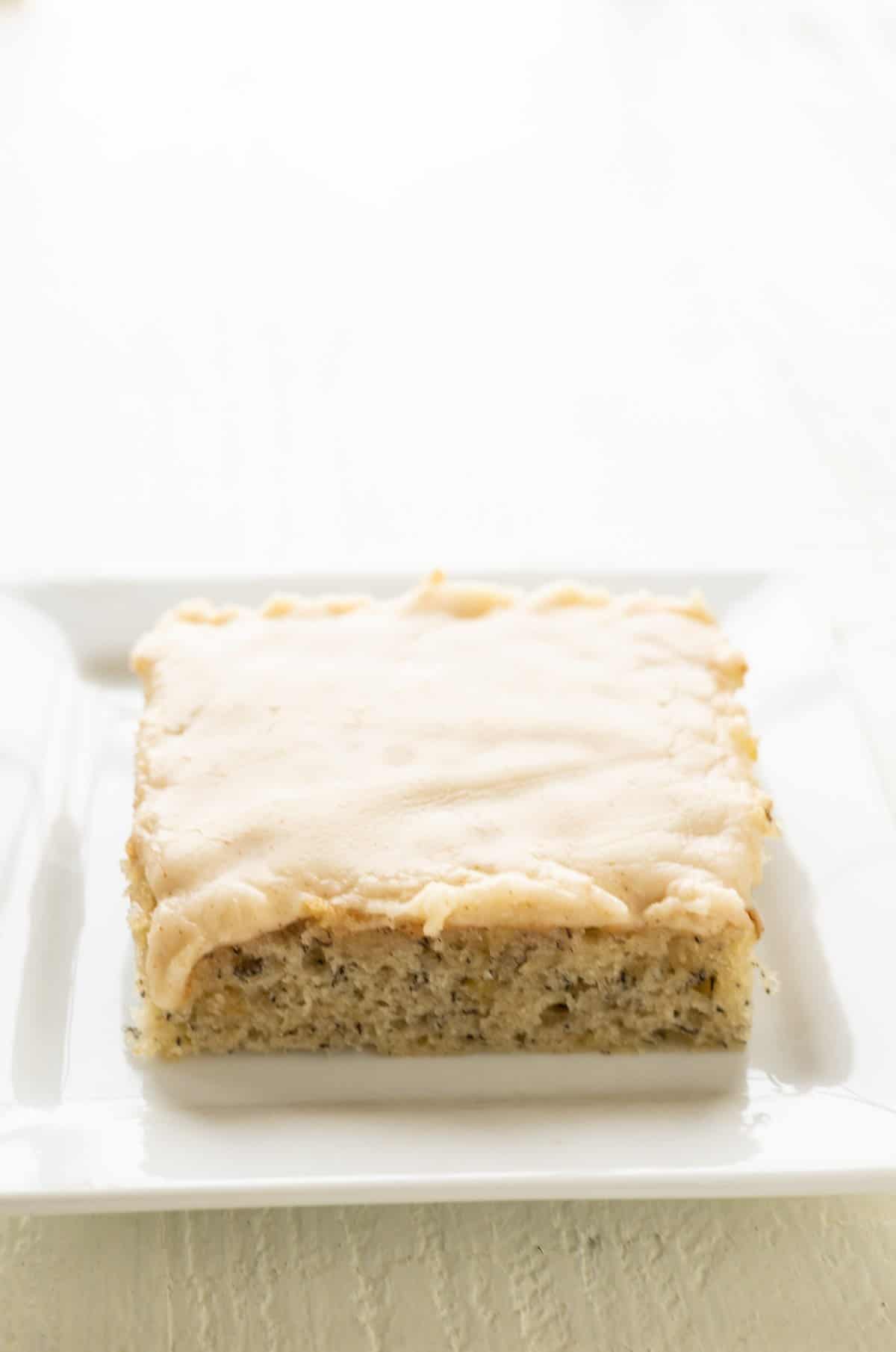 A banana square with browned butter cream cheese frosting on a plate.