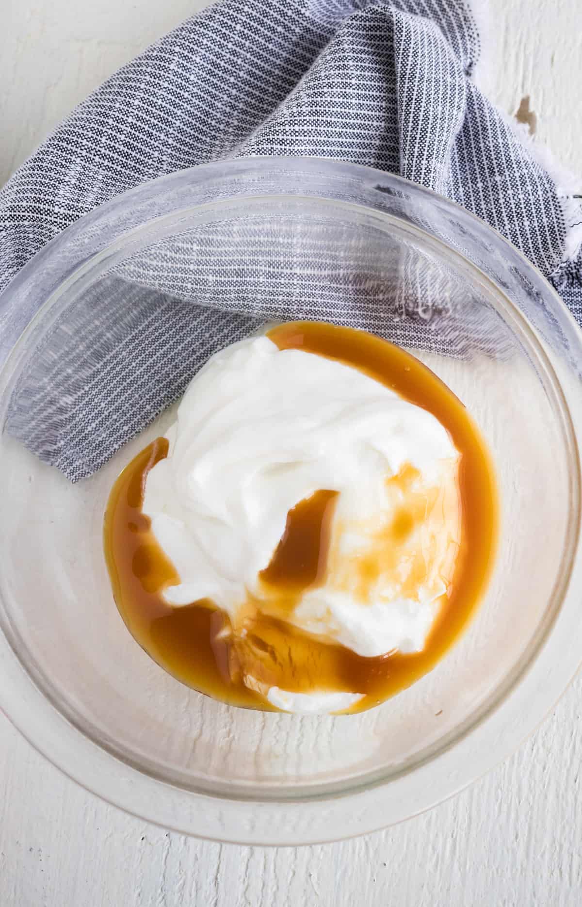 A mixing bowl with Greek yogurt, whipped cream, and caramel ice cream topping.