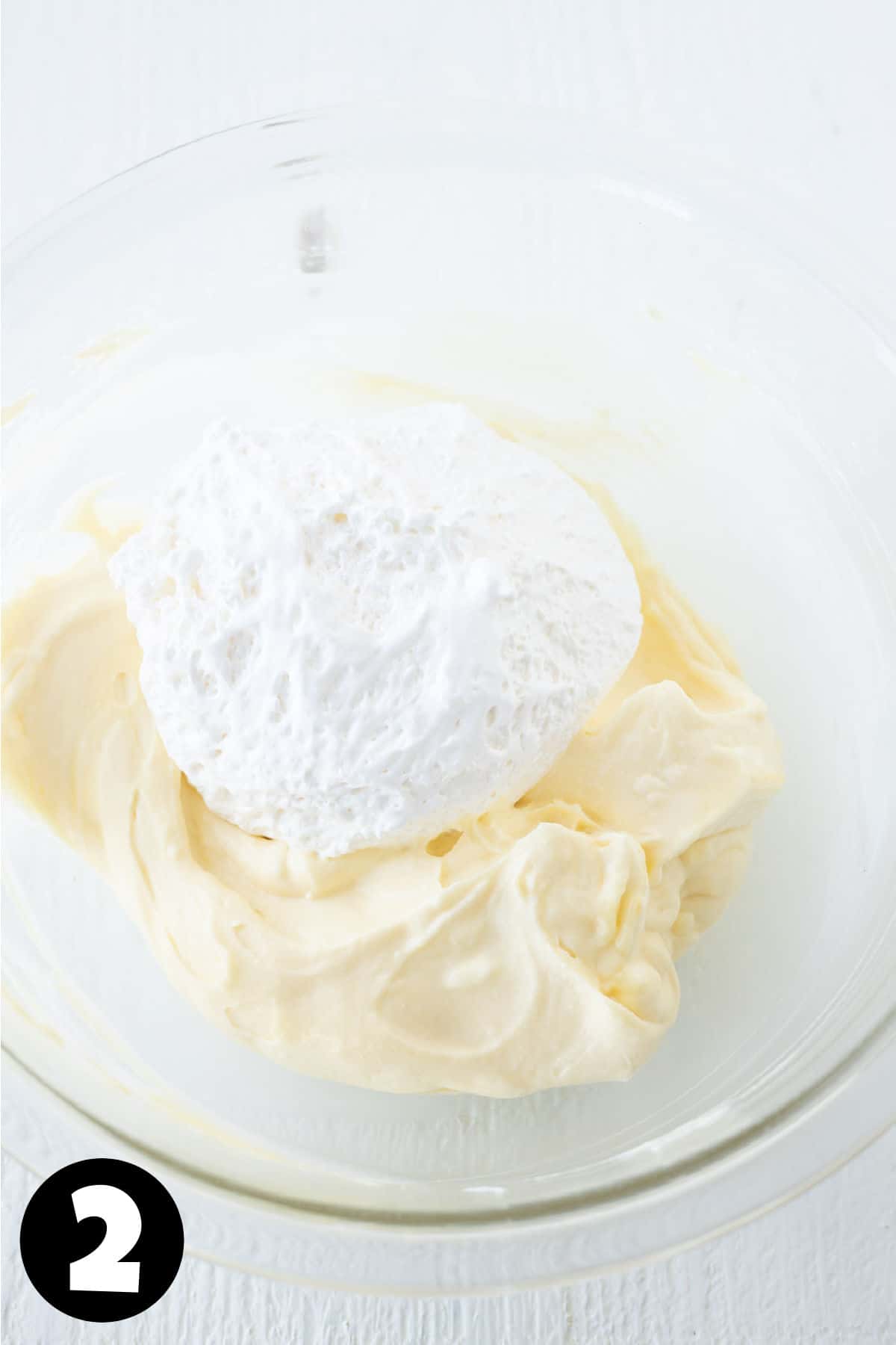 Marshmallow fluff on top of whipped cream cheese in a mixing bowl.