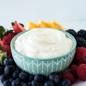 Fluffy fruit dip in a turquoise dish with strawberry, blueberry, and other fresh fruit.