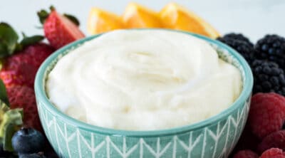 Fluffy fruit dip in a turquoise dish with strawberry, blueberry, and other fresh fruit.
