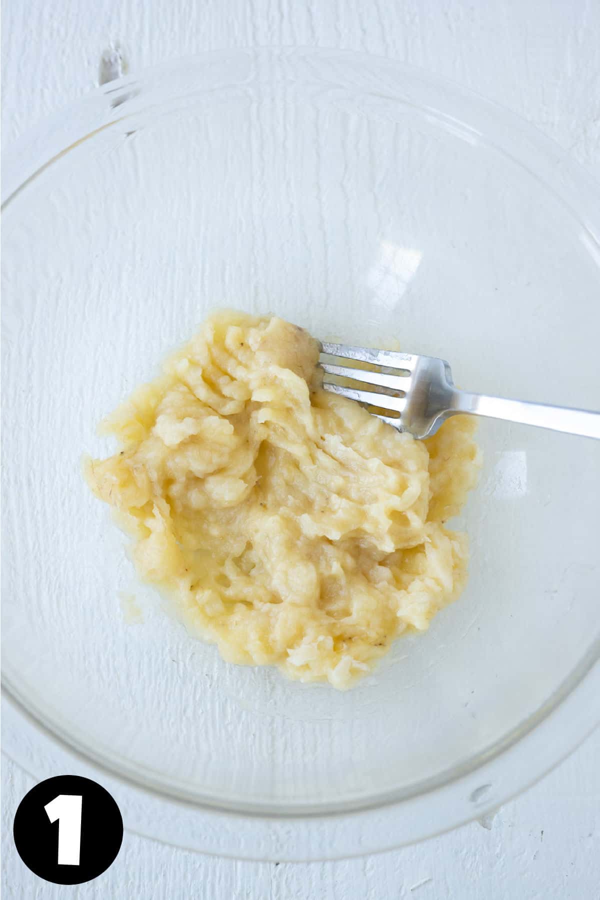 Mashed banana in a glass mixing bowl with a fork.