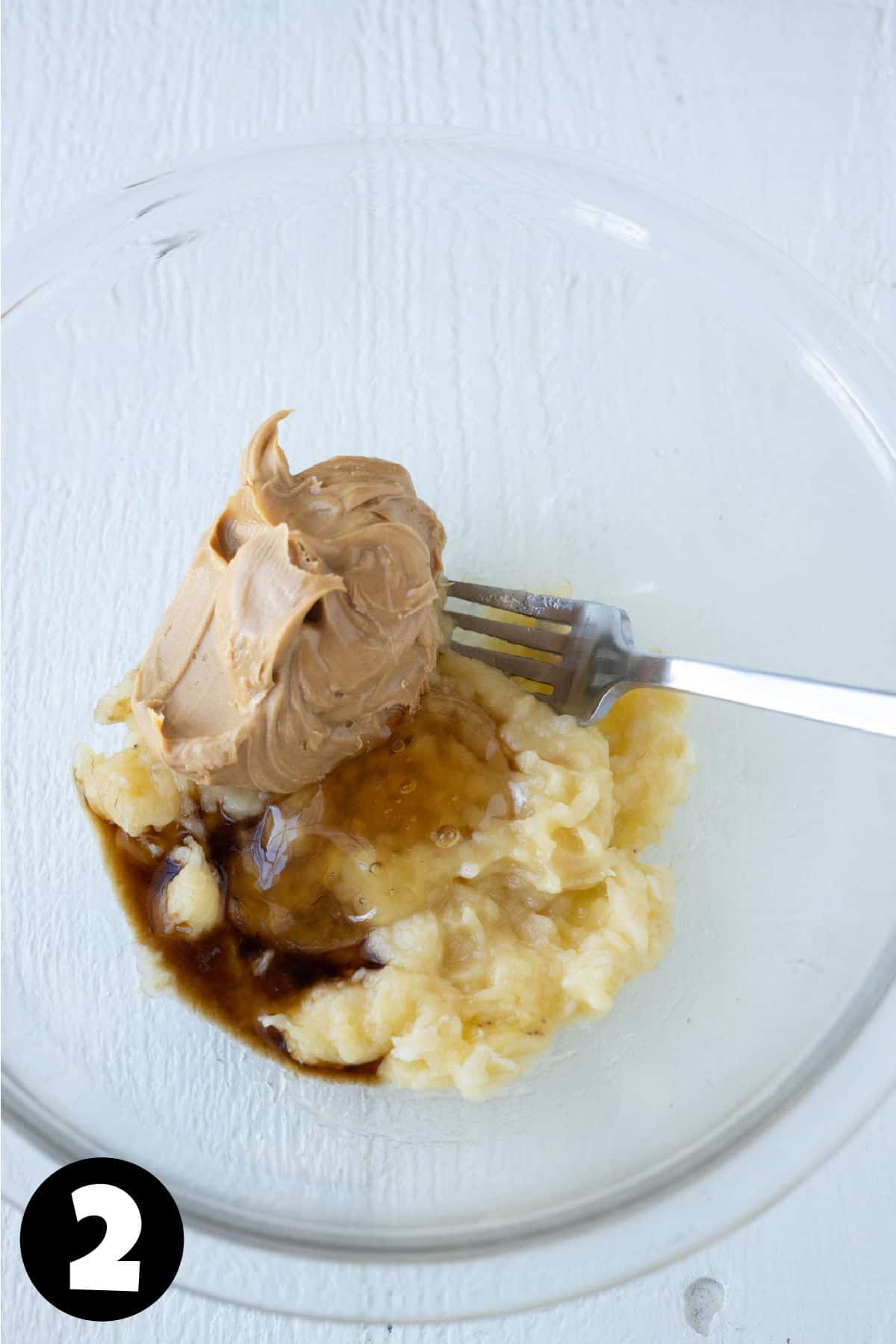 Mashed banana with peanut butter, vanilla, and honey in a mixing bowl.
