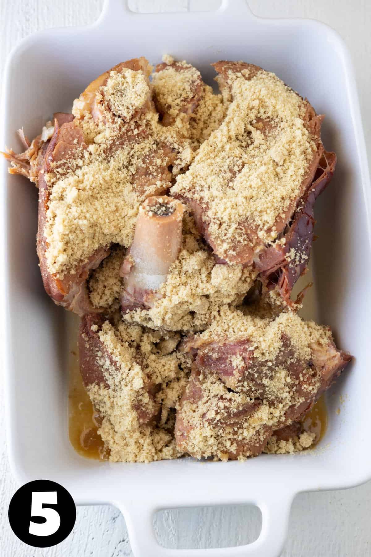 Brown sugar sprinkled over a ham in a baking dish.