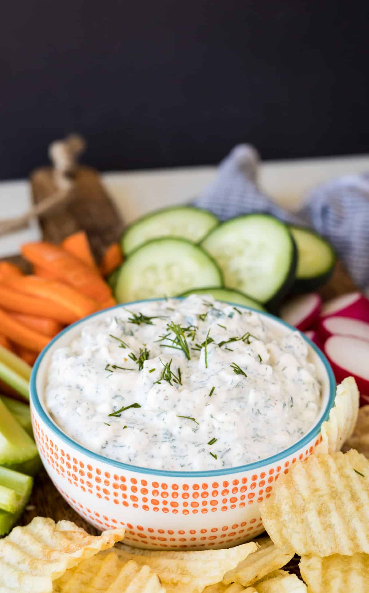 Vegetable dip in a bowl with fresh veggies and potato chips around it.