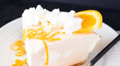 A slice of orange cheesecake garnished with orange peel and whipped cream.