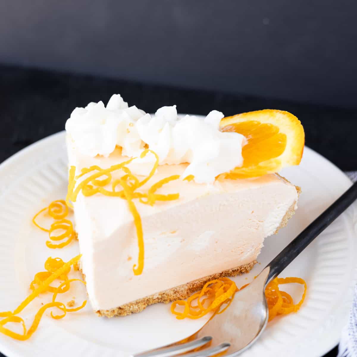 A slice of orange cheesecake garnished with orange peel and whipped cream.