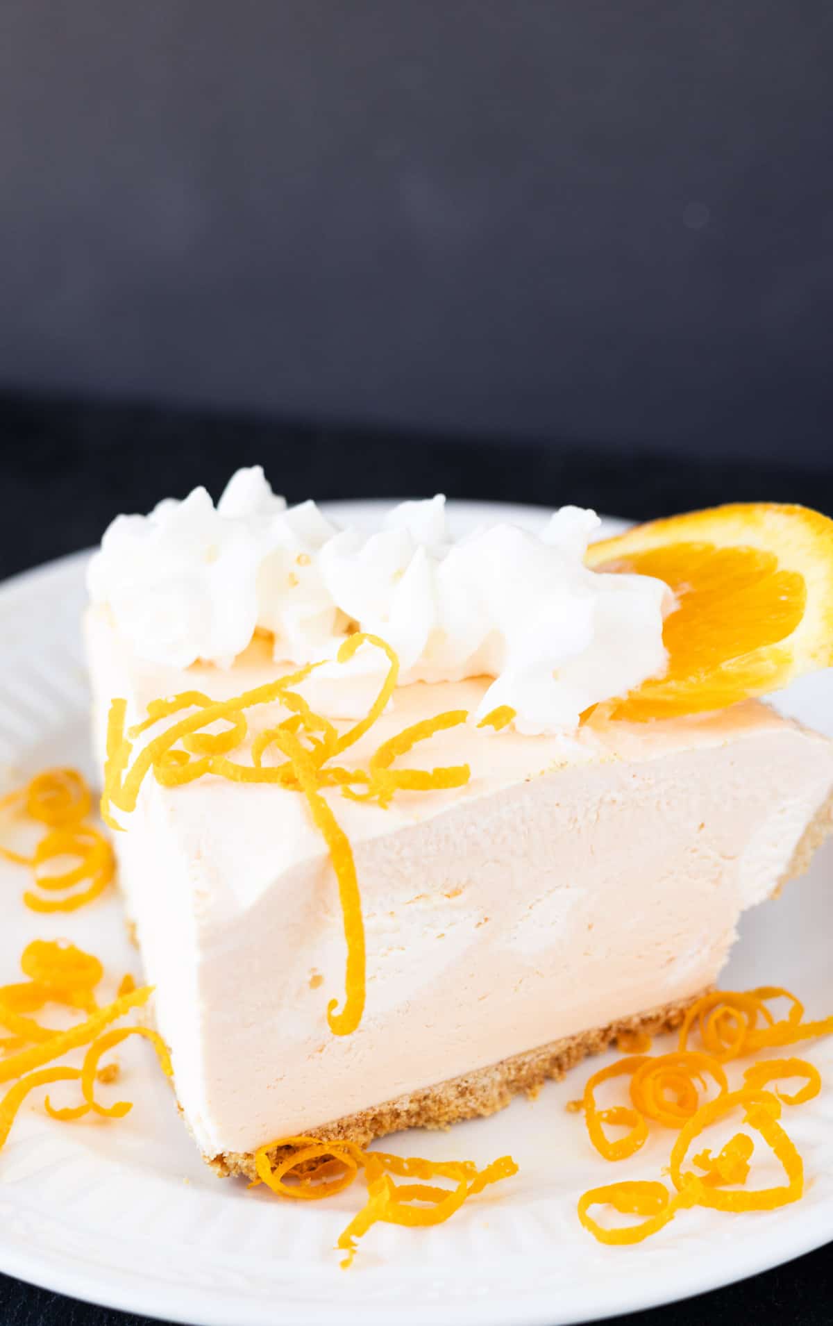 A slice of creamy orange cheesecake with orange zest and whipped cream.