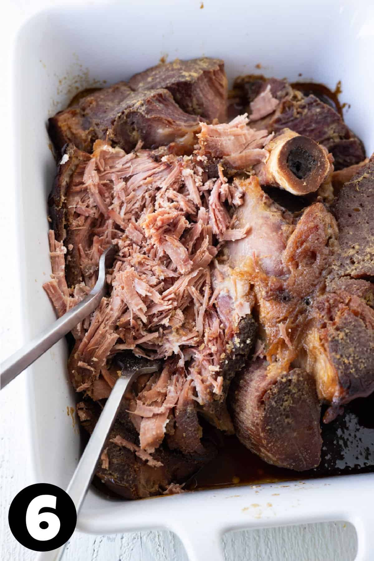 Shredded ham in a baking dish with two forks.