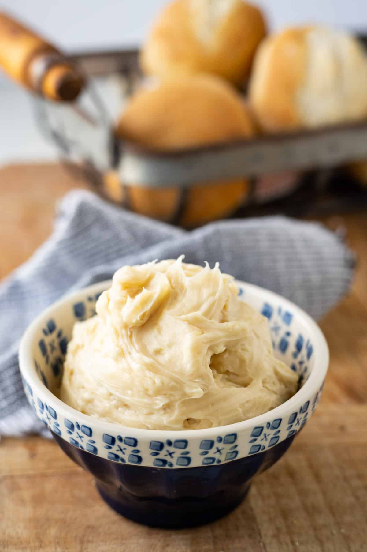 Honey butter in a blue dish with rolls in the background.