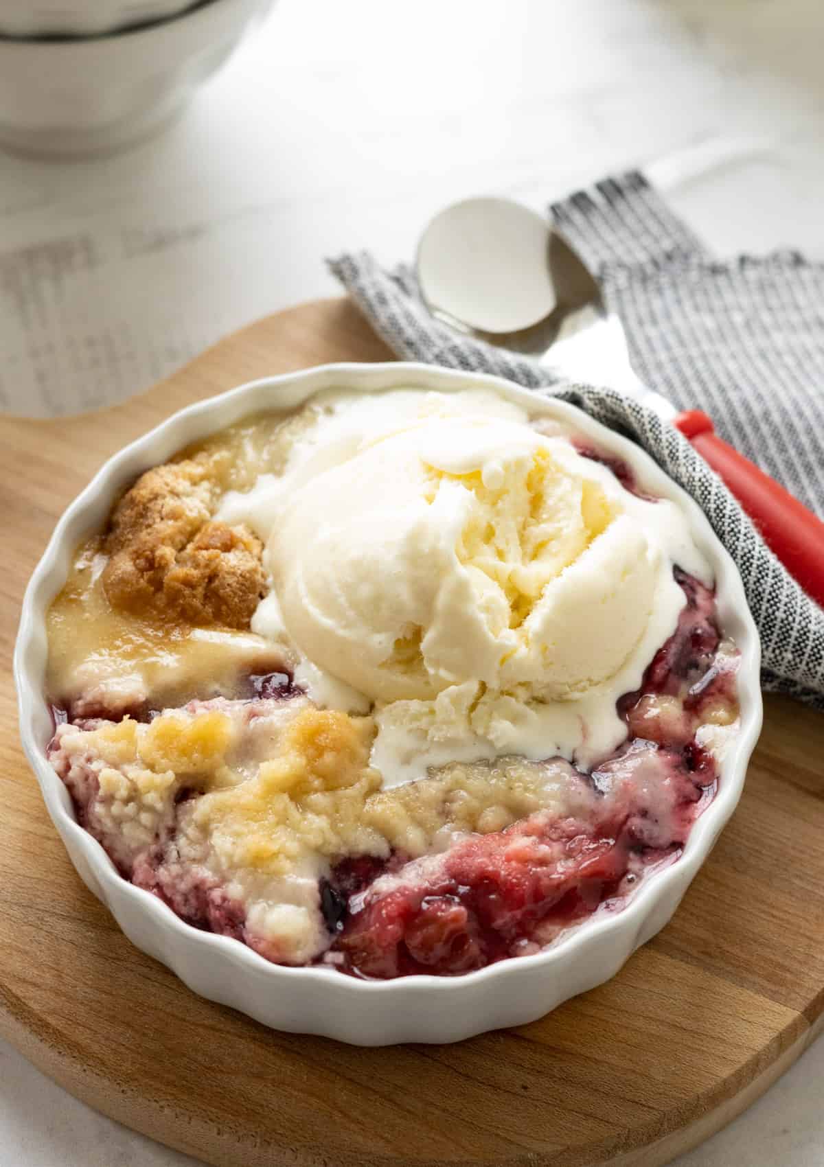 Rhubarb dump cake with vanilla ice cream in a white dish.