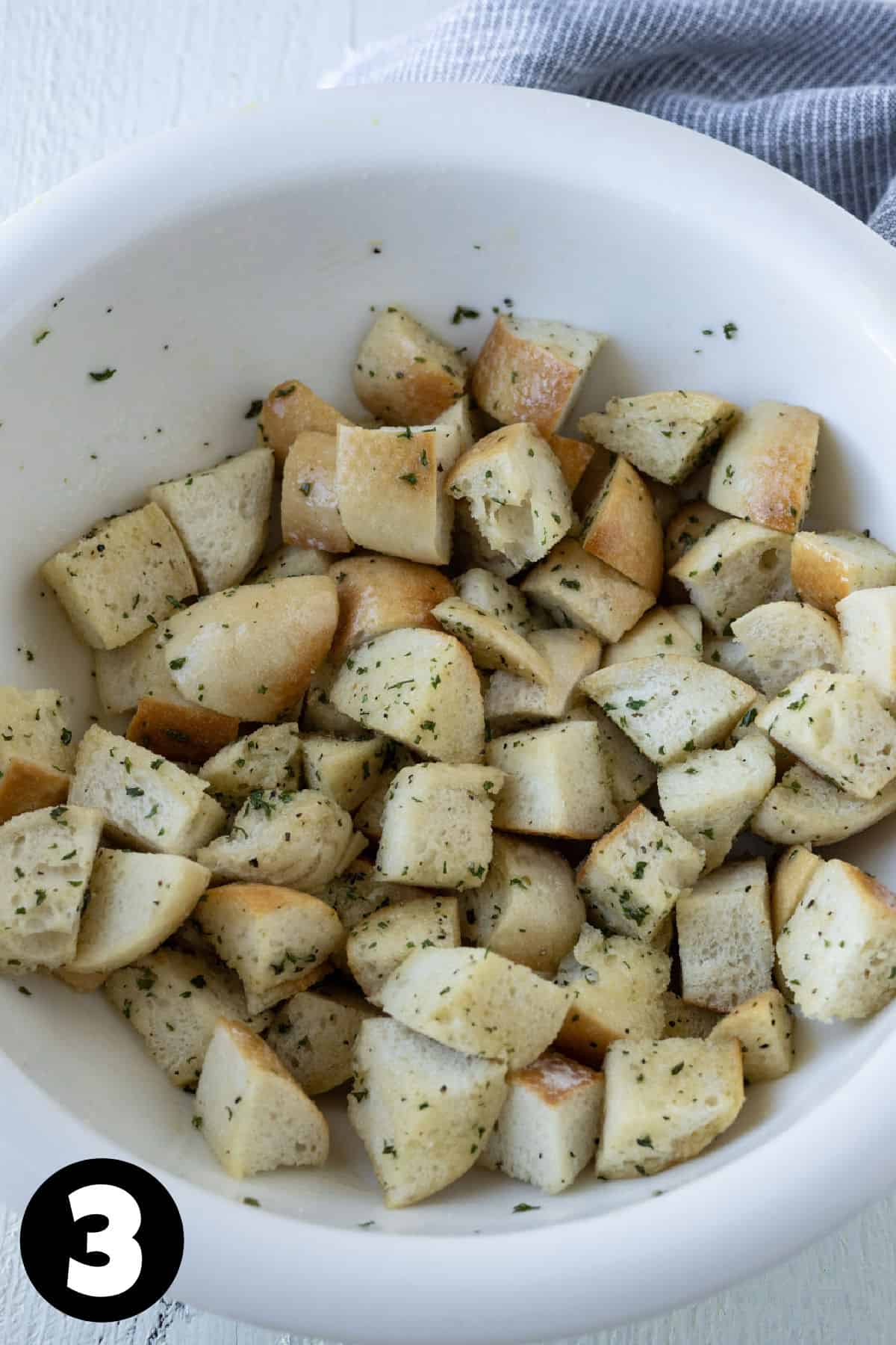 Bread cubes coated in garlic herb butter in a white bowl.