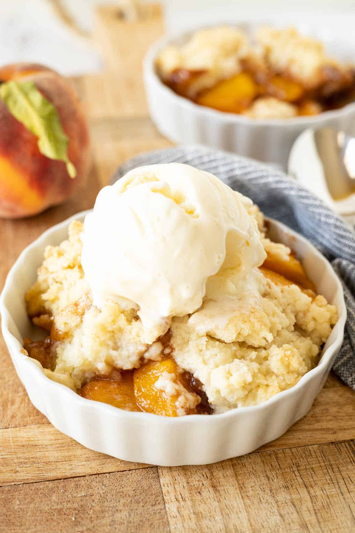 A bowl of peach cobbler with biscuit topping and vanilla ice cream.