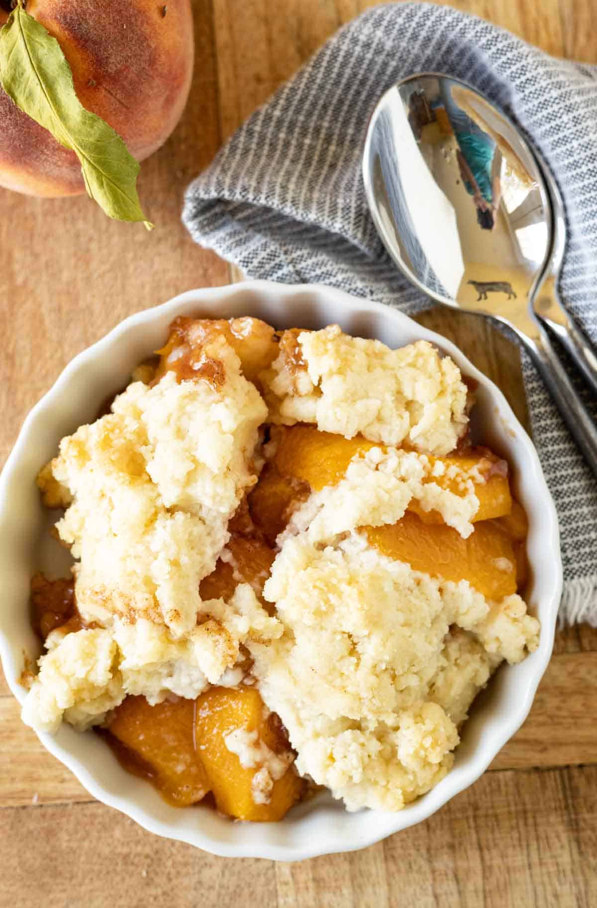 A peach cobbler topped with crust in a white dish.
