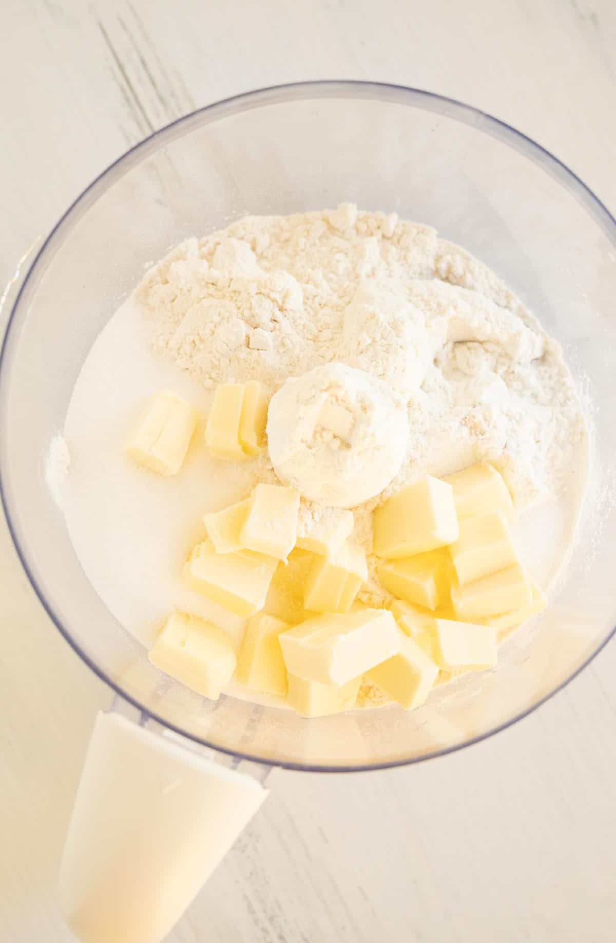 A food processor bowl with flour and butter.