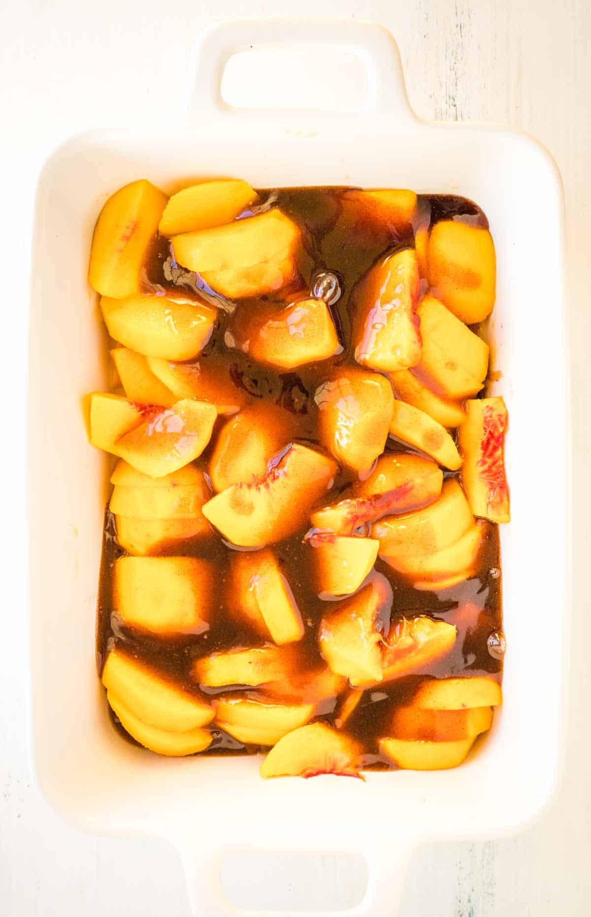 A baking dish with sliced peaches and cinnamon sauce. 