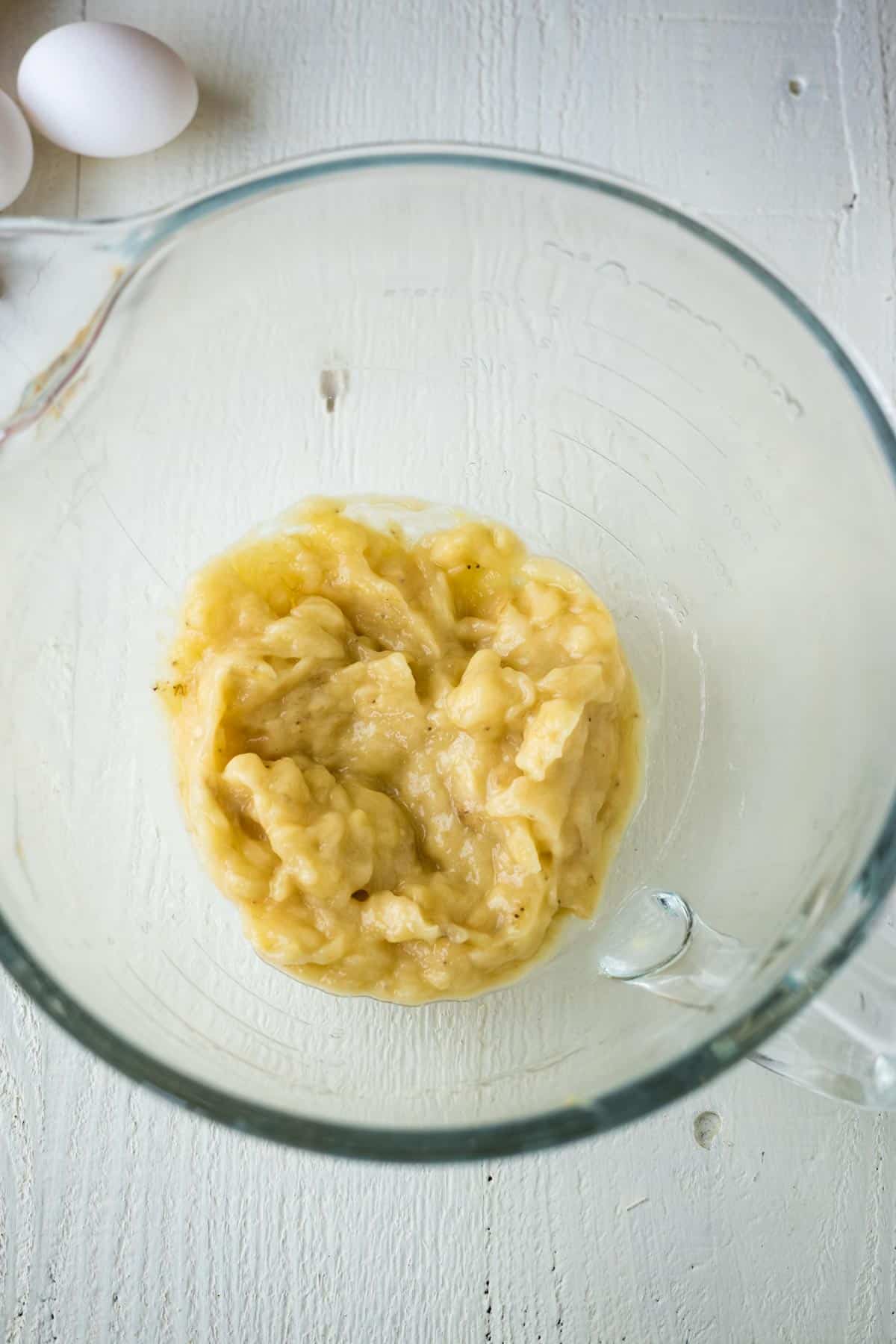 Smashed bananas in a glass mixing bowl.