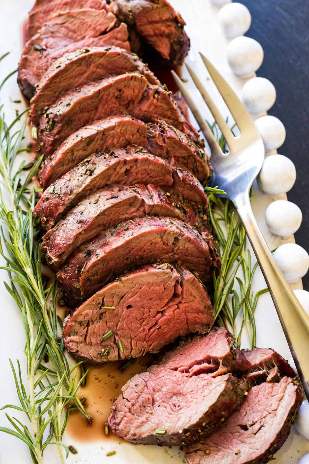 A smoked beef tenderloin cut into thick slices with fresh rosemary on the side.