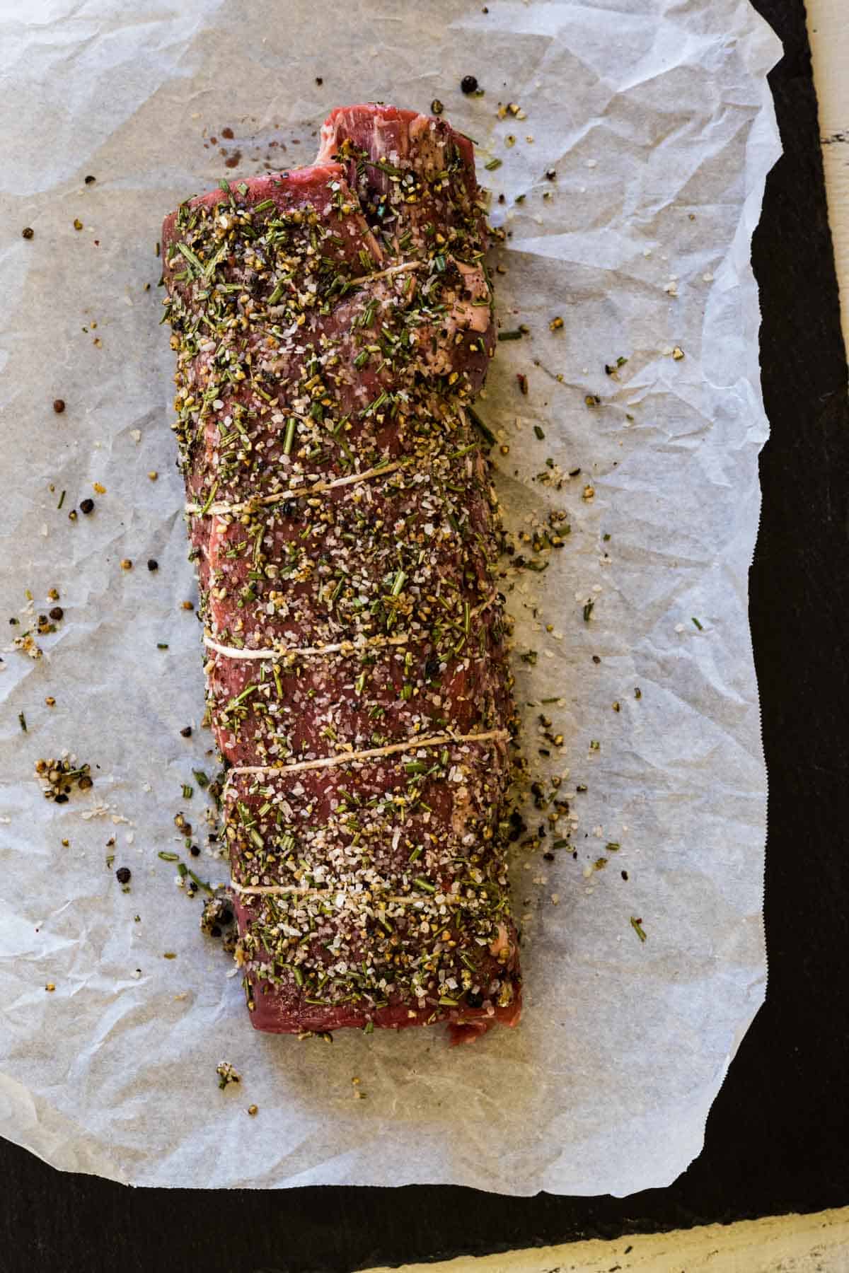 An uncooked beef tenderloin rubbed with pepper and herbs.