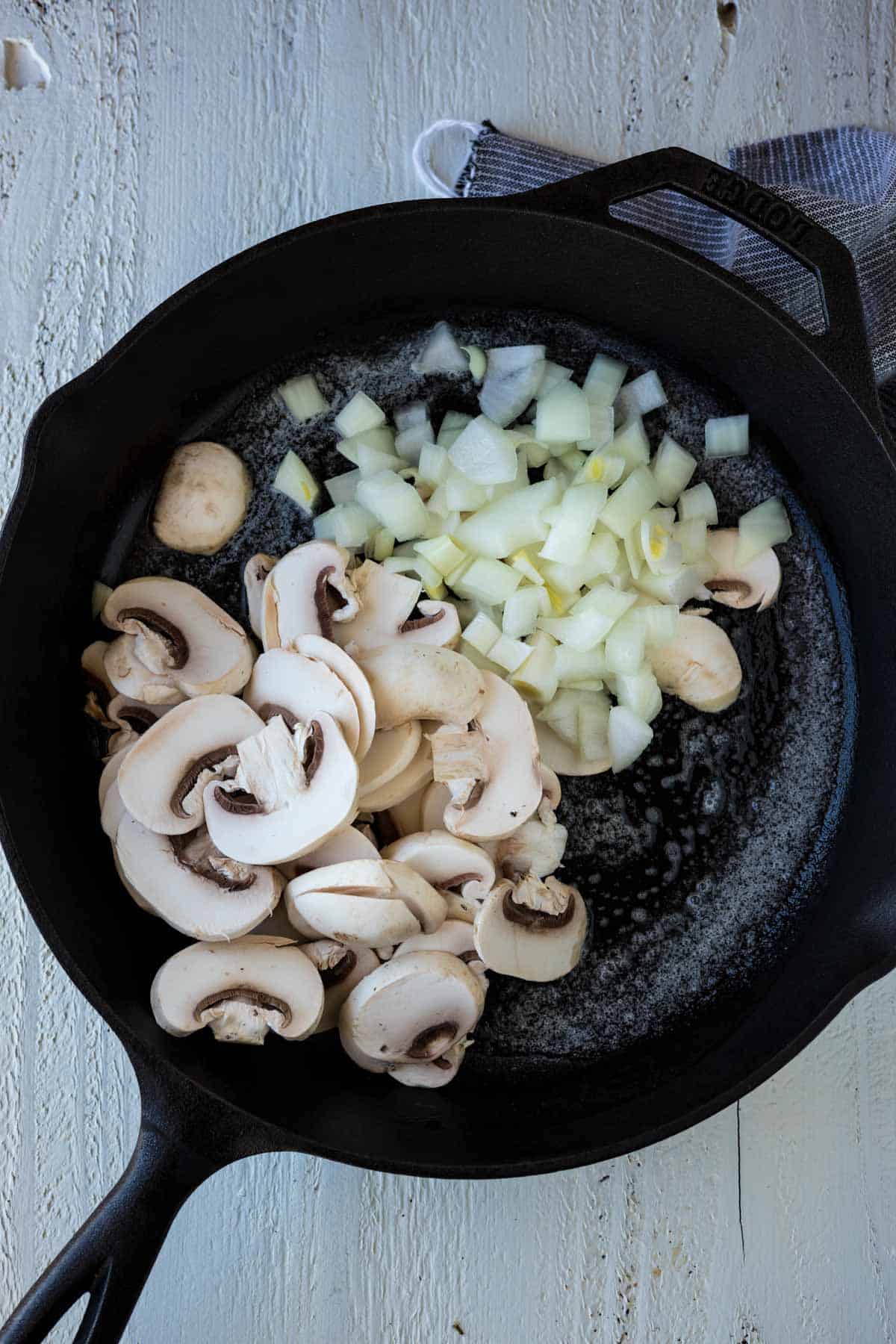 Sliced mushrooms and onions in a cast iron skillet to saute.