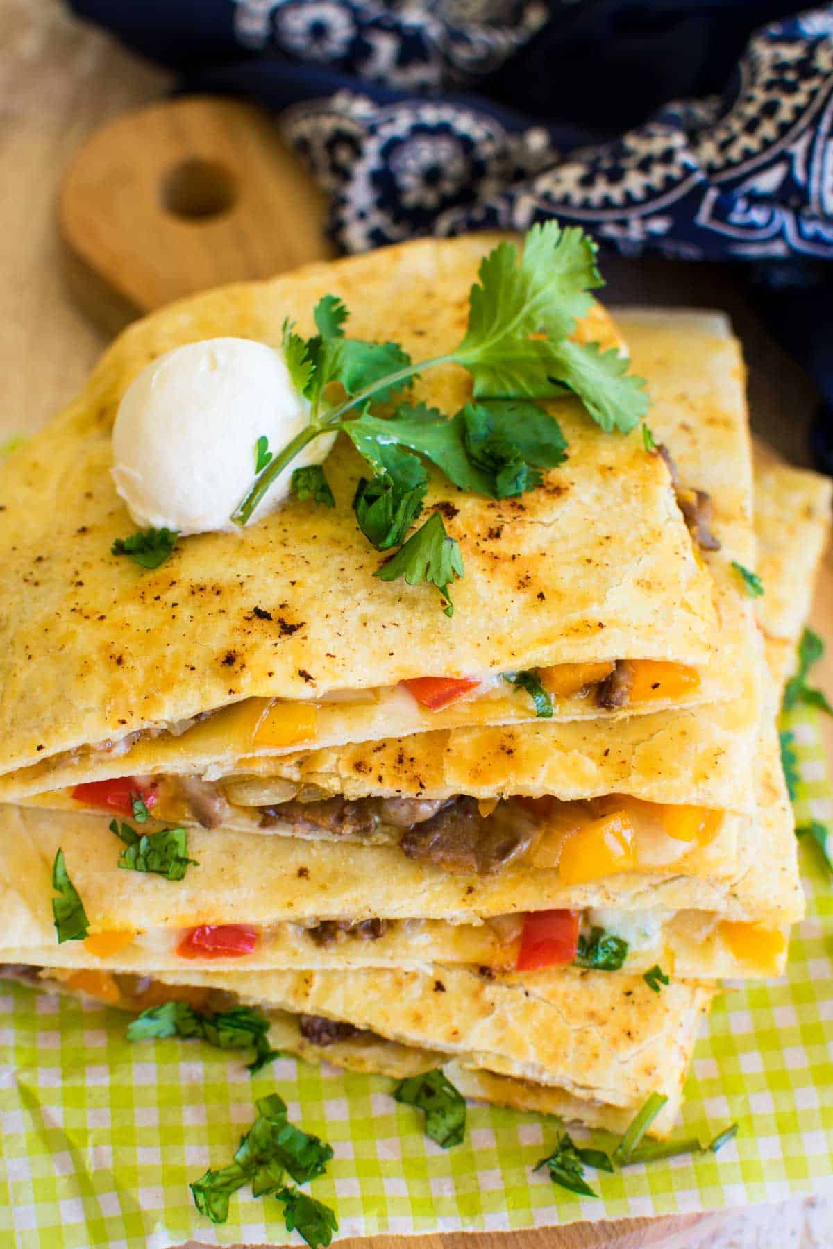 Wedges of fried cheese and steak quesadilla on a plate with sour cream and cilantro.