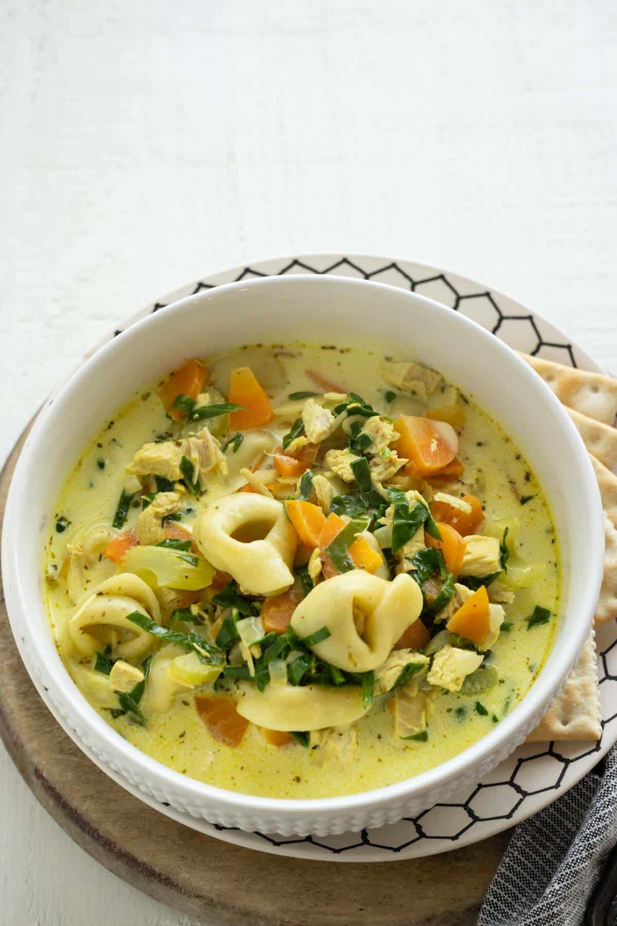A bowl of chicken tortellini soup with carrots and spinach in a creamy broth.